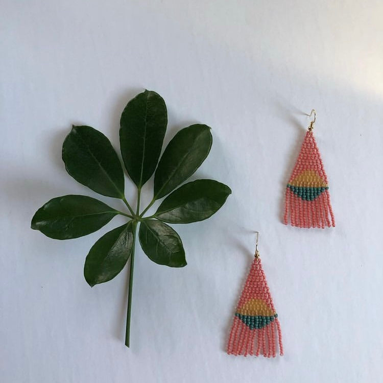 Métis hand-beaded earrings, on a white backdrop, next to a leaf.